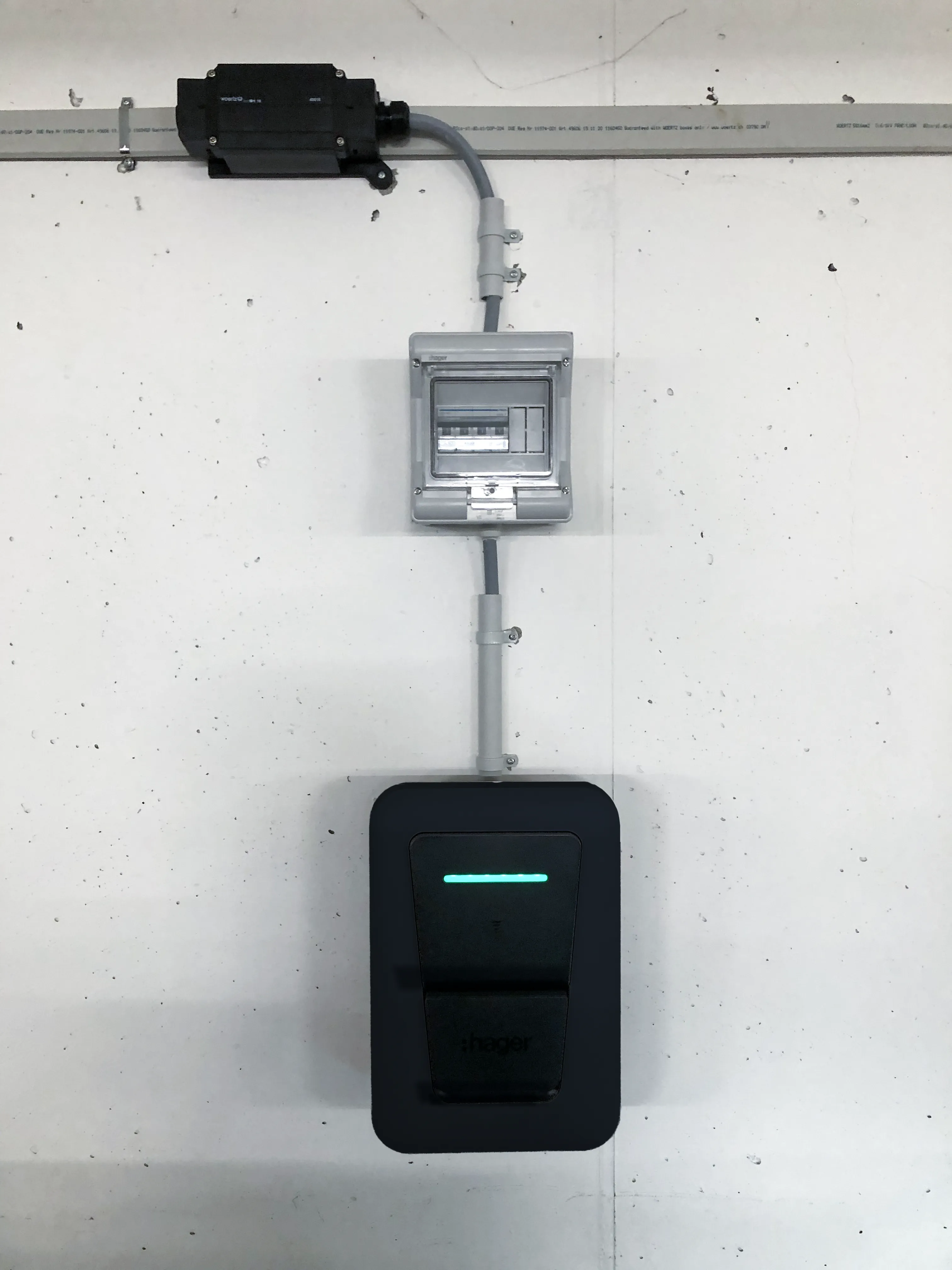 Borne de recharge Hager Witty Pro noire installée au mur sous un coffret électrique